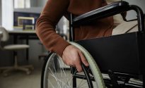 Close up of unrecognizable man with disability using wheelchair in office focus on hands turning wheel, copy space