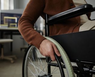 Close up of unrecognizable man with disability using wheelchair in office focus on hands turning wheel, copy space