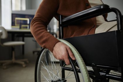 Close up of unrecognizable man with disability using wheelchair in office focus on hands turning wheel, copy space